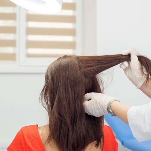 Doctor dermatologist doing hair loss test on female patient with long dark hair. Diagnostics of the hair and scalp diseases